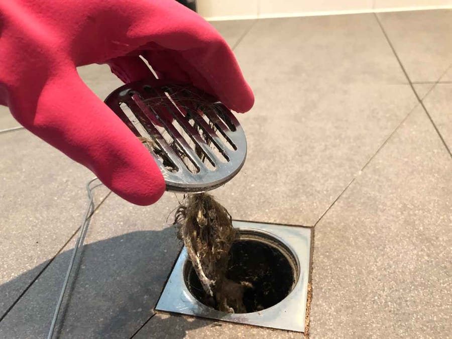 Clearing the shower drain because it is clogged with hair